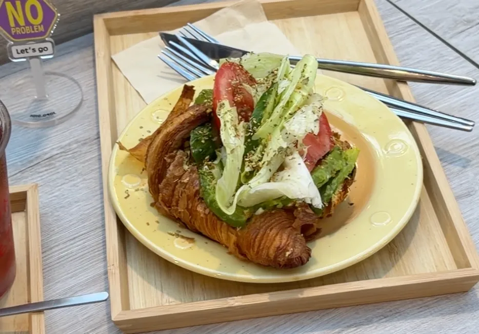 Eunice cafe 的手工可頌三明治,酥脆可頌夾著酪梨、番茄與生菜,盛在黃色圓盤上