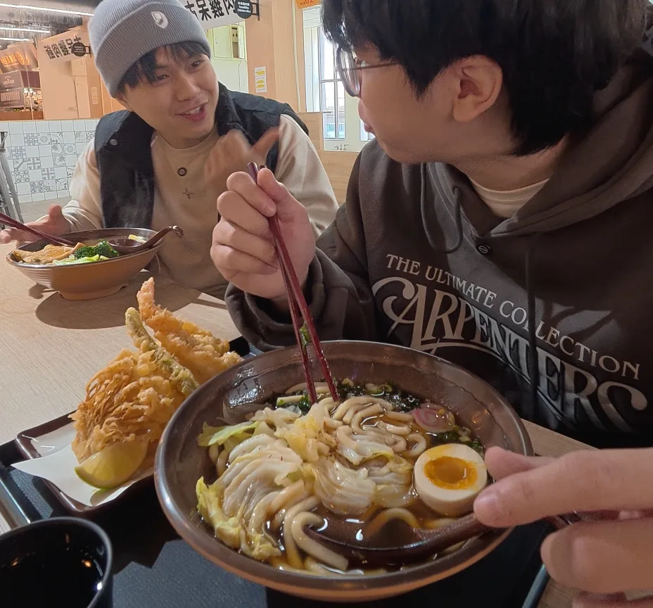 在盛匠和食吃烏龍麵,碗裡有 Q 彈烏龍麵、溏心蛋、魚板與高麗菜,旁邊擺著天婦羅