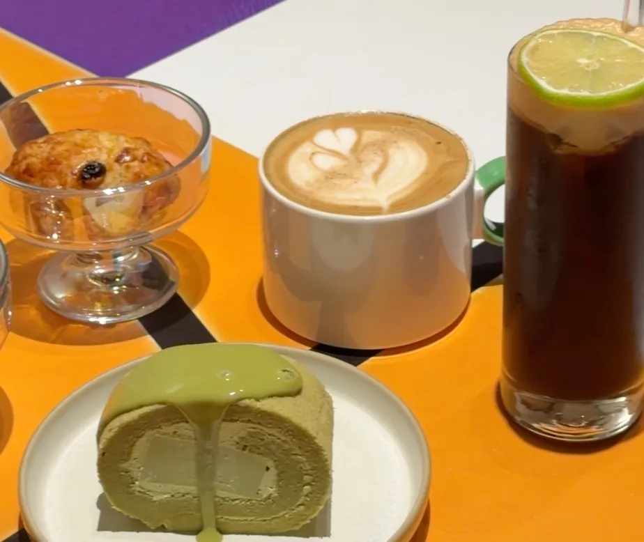 向島咖啡的甜點與飲料,甜司康、拉花拿鐵、加了檸檬片的西西里咖啡與淋醬的碧螺春乳卷,擺在彩色幾何桌面上